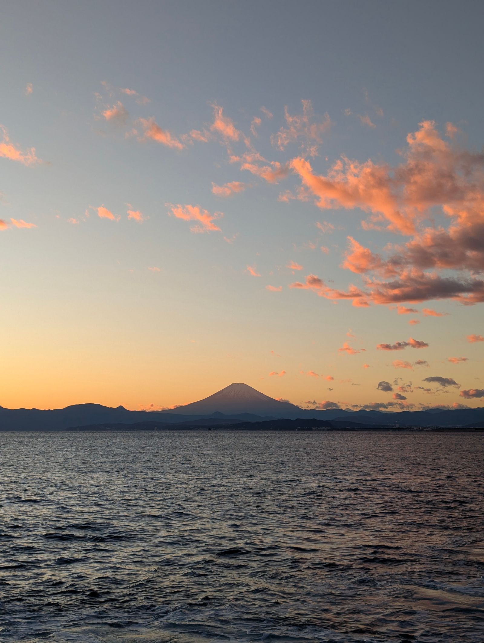 Sunset over the sea with Mount Fuji silhouetted against a pink and orange sky